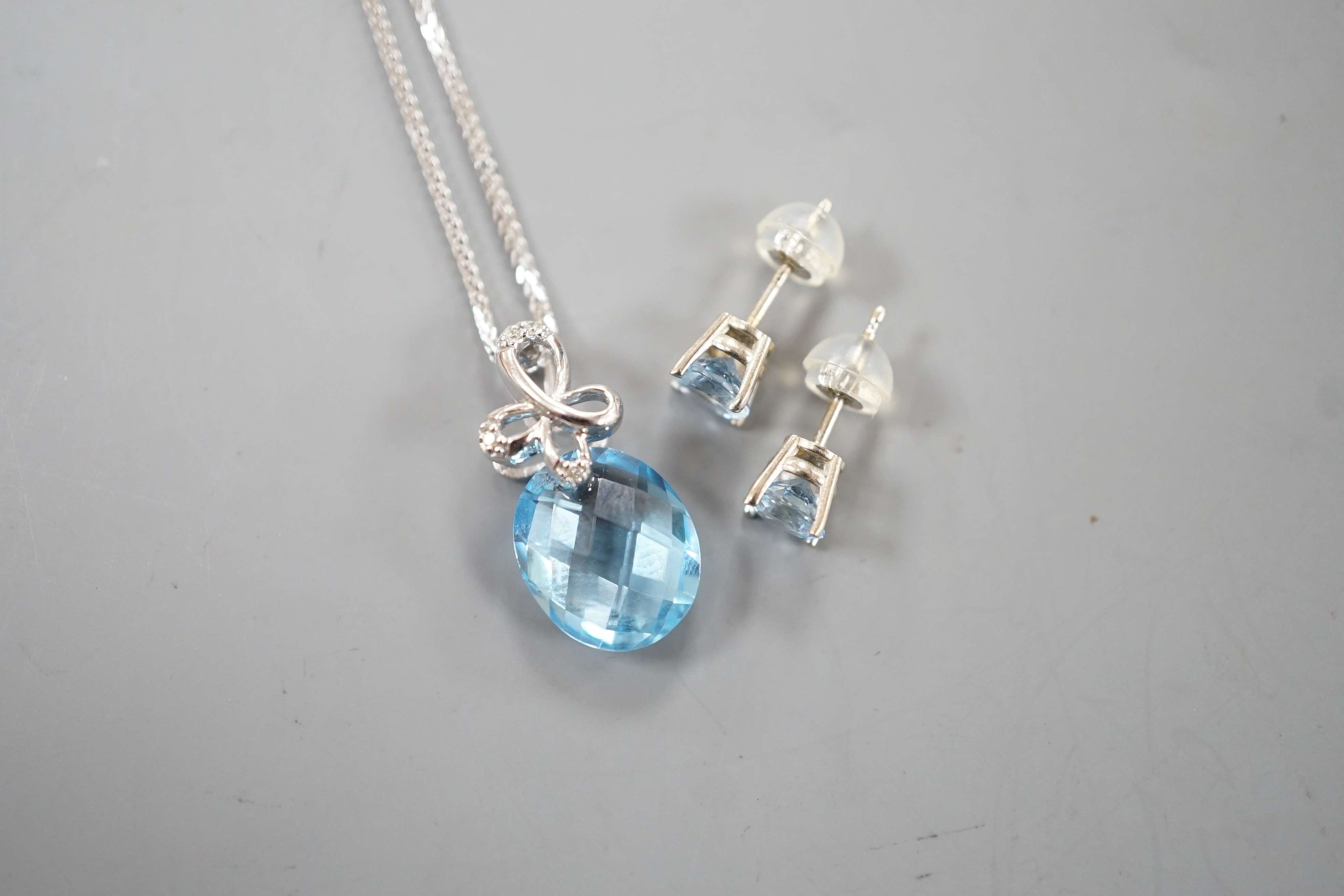 A modern 14k white metal, facetted pear cut blue topaz and diamond chip set pendant, 19mm, on a 750 white metal chain, 44cm and a pair 14k and blue topaz ear studs, gross weight 5.1 grams.
